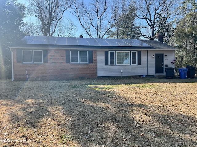 ranch-style home with brick siding, a chimney, solar panels, crawl space, and a front lawn