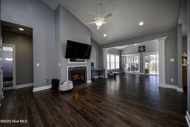 unfurnished living room featuring ceiling fan, a premium fireplace, wood finished floors, baseboards, and ornate columns