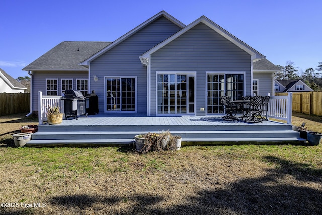 back of house with roof with shingles, fence, a deck, and a lawn