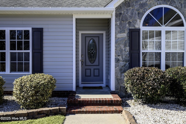 doorway to property featuring stone siding and a shingled roof