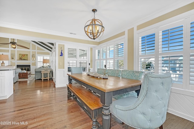 dining space with crown molding, visible vents, wood finished floors, and a glass covered fireplace