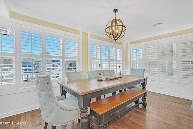 dining space with an inviting chandelier, visible vents, ornamental molding, and wood finished floors