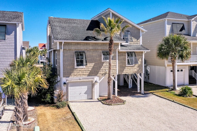 coastal inspired home with a carport, driveway, a shingled roof, and an attached garage