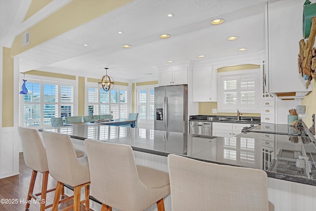 kitchen featuring decorative light fixtures, stainless steel appliances, dark countertops, white cabinetry, and a sink