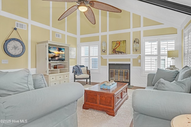 living area featuring high vaulted ceiling, a glass covered fireplace, visible vents, and ceiling fan