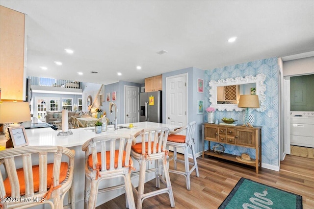 kitchen featuring light wood-style flooring, a peninsula, a sink, washer / clothes dryer, and stainless steel fridge