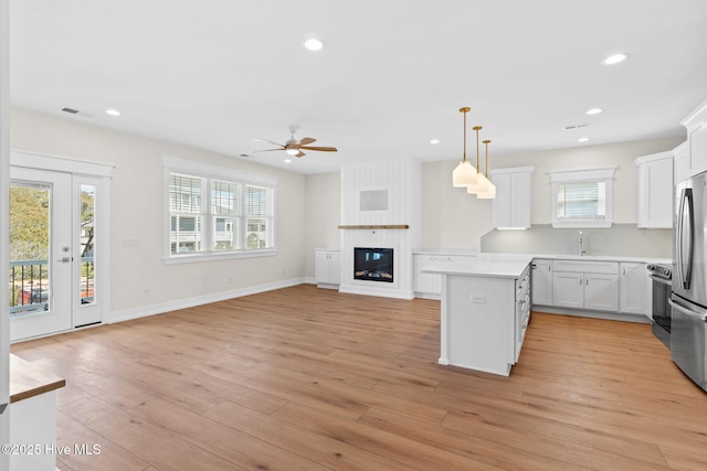 kitchen featuring light wood finished floors, white cabinets, light countertops, a fireplace, and a sink