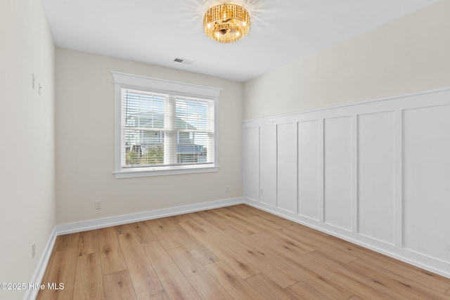 spare room featuring light wood finished floors, baseboards, visible vents, and a decorative wall