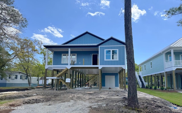 coastal home featuring a carport, a porch, stairs, and dirt driveway