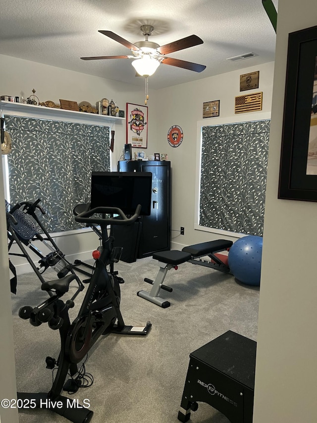 exercise area with visible vents, a textured ceiling, carpet, and a ceiling fan