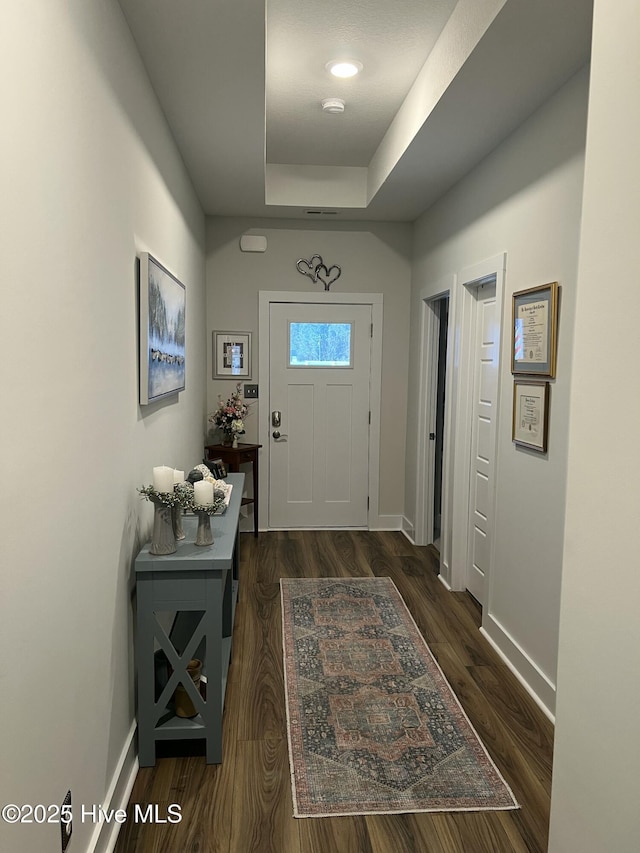 entrance foyer featuring a tray ceiling, dark wood-style floors, and baseboards