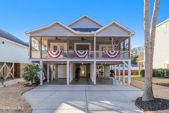 coastal home featuring a ceiling fan, driveway, roof with shingles, stairway, and a carport