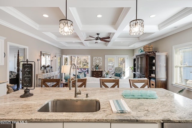 kitchen featuring light stone counters, open floor plan, a sink, and hanging light fixtures