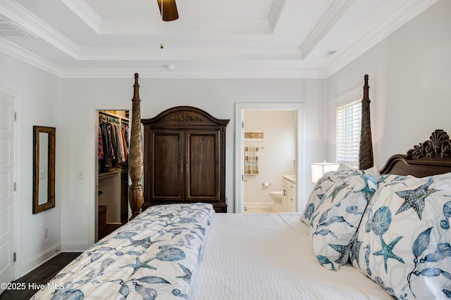 bedroom featuring wood finished floors, visible vents, a closet, a tray ceiling, and a walk in closet