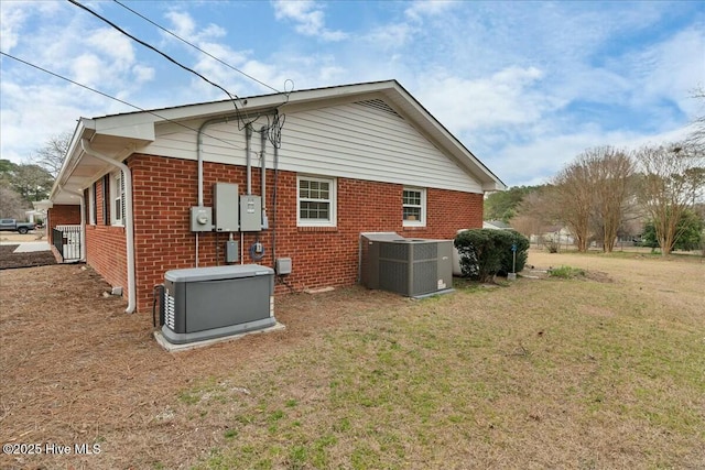 back of property featuring brick siding, central AC unit, and a lawn