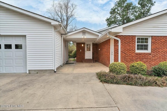 view of exterior entry with a garage, brick siding, and driveway