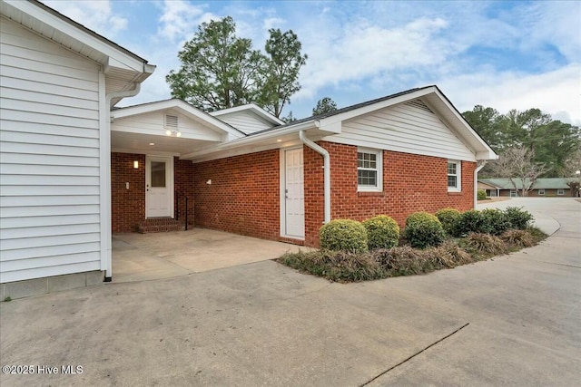 view of side of home with an attached carport, brick siding, concrete driveway, and entry steps