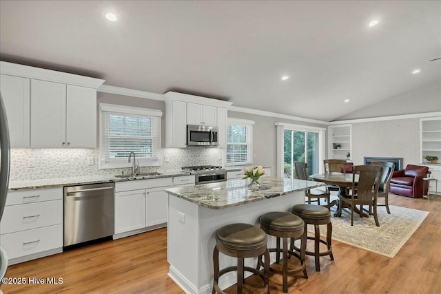 kitchen with a kitchen island, a fireplace, a sink, stainless steel appliances, and light wood-type flooring