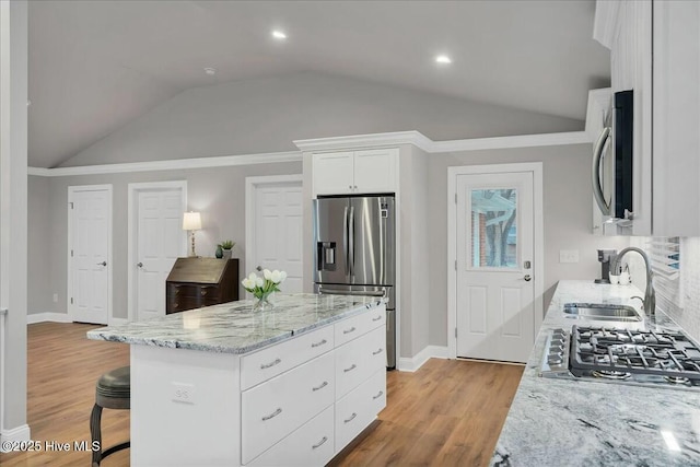 kitchen featuring a sink, light stone counters, light wood-style floors, appliances with stainless steel finishes, and vaulted ceiling