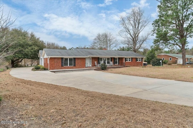 ranch-style home featuring brick siding, driveway, a chimney, and a front lawn