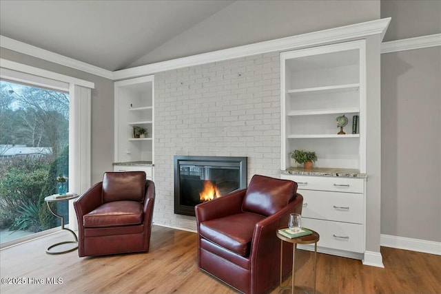 sitting room with built in shelves, light wood-style flooring, a fireplace, and vaulted ceiling