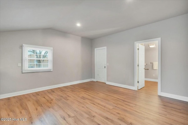 spare room featuring lofted ceiling, baseboards, and light wood-type flooring