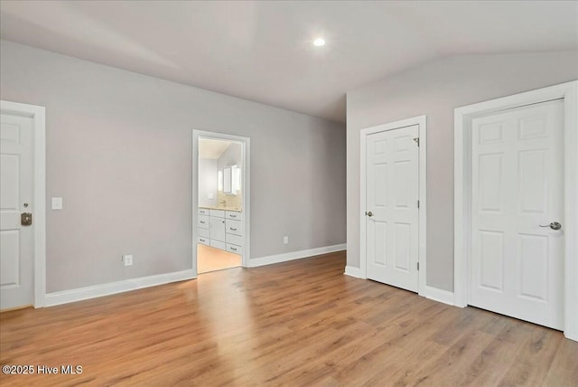 unfurnished bedroom featuring baseboards, ensuite bath, vaulted ceiling, and light wood finished floors