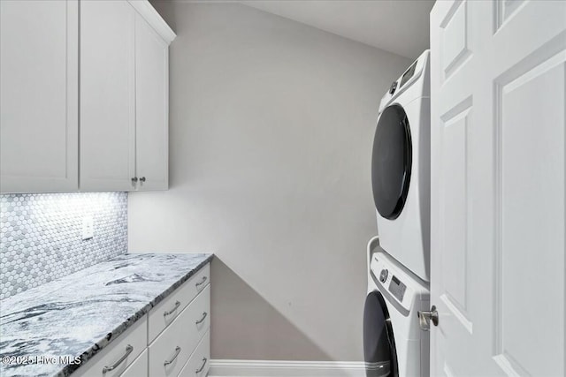 washroom with stacked washer / drying machine, cabinet space, and baseboards