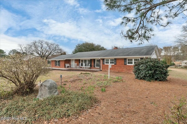 view of front of property featuring brick siding, a porch, and a chimney