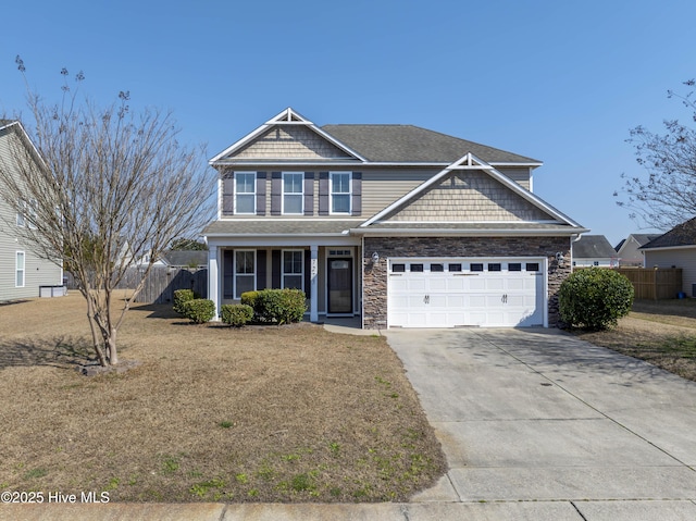 view of front of home featuring driveway, stone siding, an attached garage, fence, and a front yard