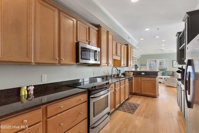 kitchen with light wood finished floors, open floor plan, a peninsula, stainless steel appliances, and a sink