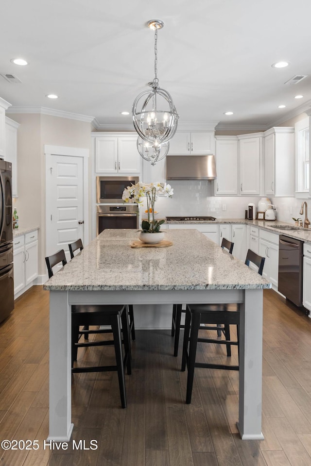 935 Baldwin Park Dr, Wilmington, NC 28411 - kitchen with appliances with stainless steel finishes, under cabinet range hood, a breakfast bar, ornamental molding, and a kitchen island