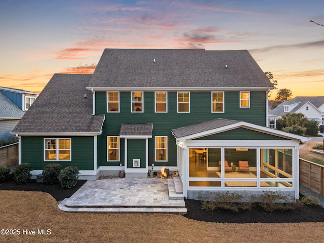 back of house with fence, a shingled roof, a sunroom, and a patio