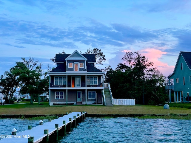 back of property at dusk with central air condition unit, a water view, fence, a yard, and stairway