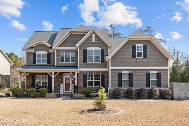 view of front of property with covered porch, stone siding, a shingled roof, and fence