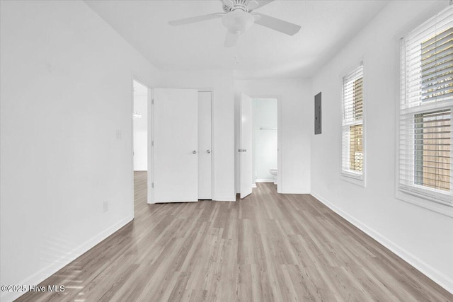 unfurnished bedroom featuring ceiling fan, connected bathroom, wood finished floors, electric panel, and baseboards