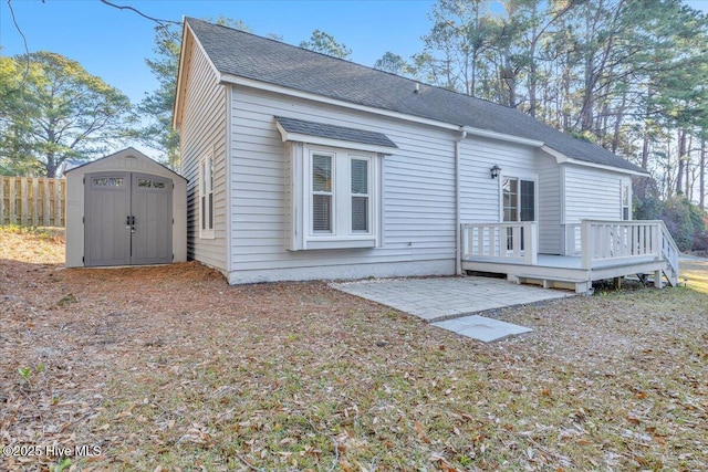 rear view of property featuring an outbuilding, fence, a deck, a patio area, and a shed