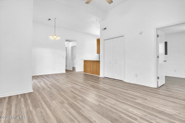 unfurnished living room featuring visible vents, baseboards, a towering ceiling, light wood-type flooring, and ceiling fan with notable chandelier