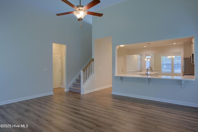 unfurnished living room featuring ceiling fan with notable chandelier, dark wood-style flooring, a sink, baseboards, and stairway