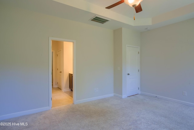 unfurnished bedroom with connected bathroom, light carpet, visible vents, baseboards, and a tray ceiling