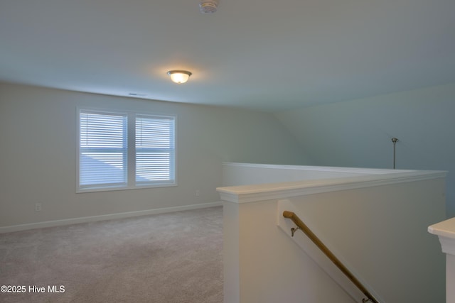 interior space featuring lofted ceiling, baseboards, light colored carpet, and an upstairs landing