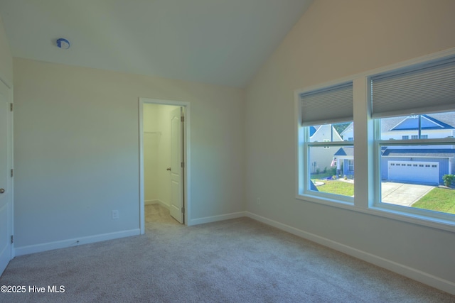 unfurnished room featuring light carpet, vaulted ceiling, and baseboards