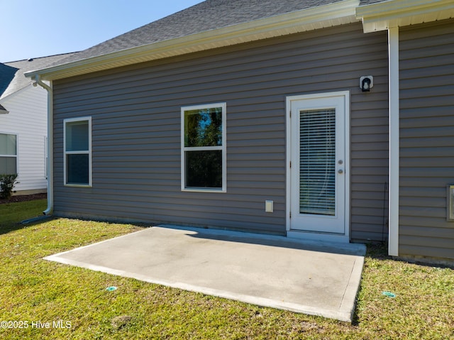 back of property with a shingled roof, a yard, and a patio