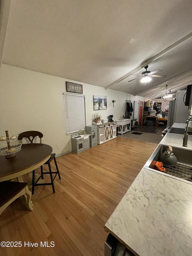 kitchen with a ceiling fan, a sink, a textured ceiling, and wood finished floors