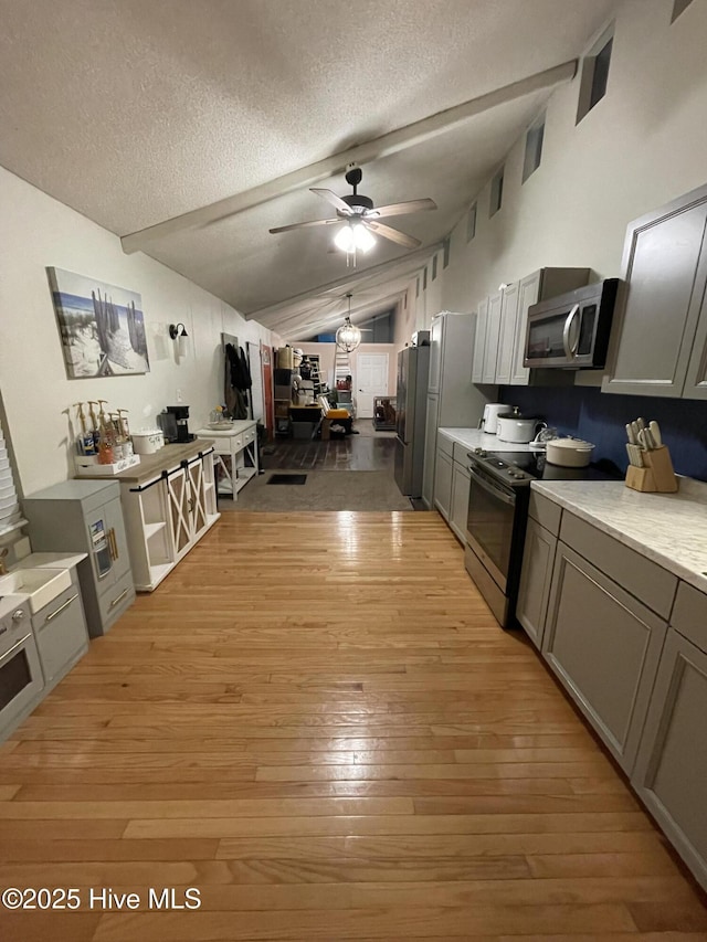 kitchen with vaulted ceiling with beams, light countertops, light wood-type flooring, electric range oven, and stainless steel microwave