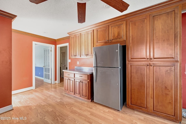 kitchen with a ceiling fan, light wood-style flooring, freestanding refrigerator, light countertops, and crown molding