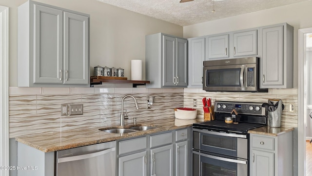 kitchen with ceiling fan, light stone counters, stainless steel appliances, a sink, and backsplash