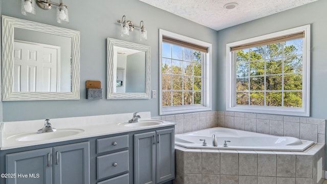 full bathroom featuring double vanity, a textured ceiling, a sink, and a bath