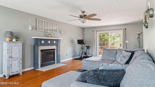 living area featuring a textured ceiling, a tile fireplace, wood finished floors, and baseboards