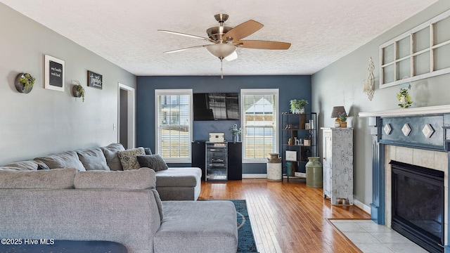 living area with a textured ceiling, a fireplace, light wood-style flooring, and a ceiling fan